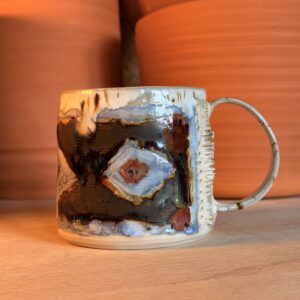 Close-up of a ceramic mug with blue and brown glaze on a wooden table, orange background.